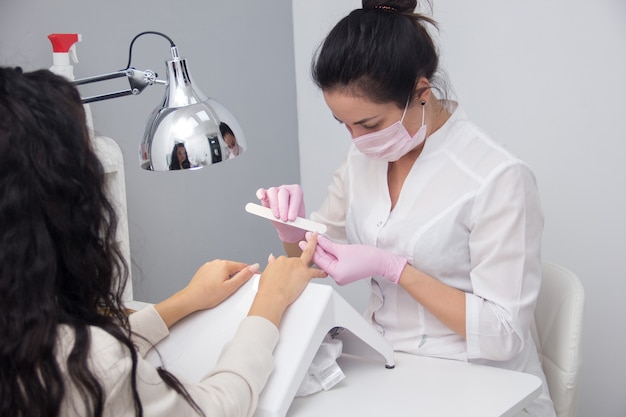 Una manicurista le da una manicura a un cliente. Retrato de una atractiva trabajadora de salón de uñas dando una manicura a uno de sus clientes habituales