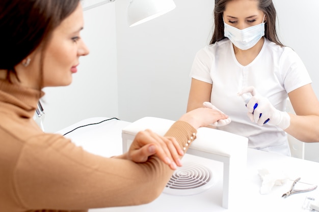 Manicurista es spray de aplicaciones en la mano del cliente.