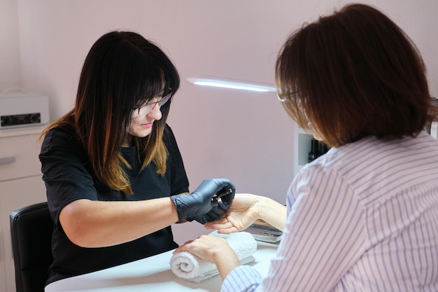 La manicurista femenina hace manicura con herramientas profesionales para el cliente en un salón de belleza para el cuidado de manos y uñas