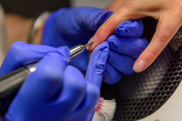 Manicurista en guantes azules quita la cutícula con un cortador