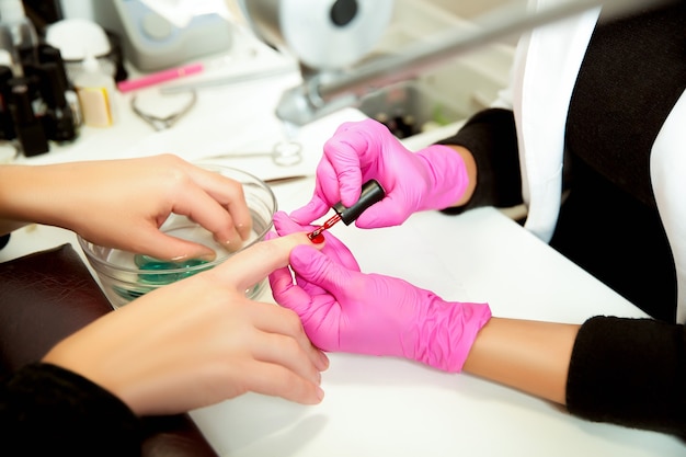 El manicurista con guantes de goma aplica un lok en las uñas. Herramienta de manicura profesional.