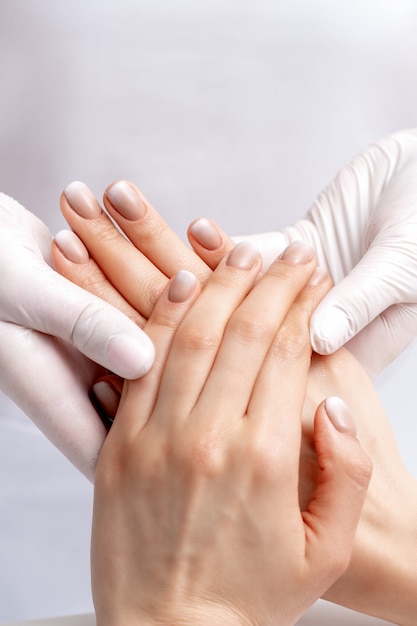 Manicurista con guantes haciendo masaje de cera en manos femeninas con manicura en salón de uñas