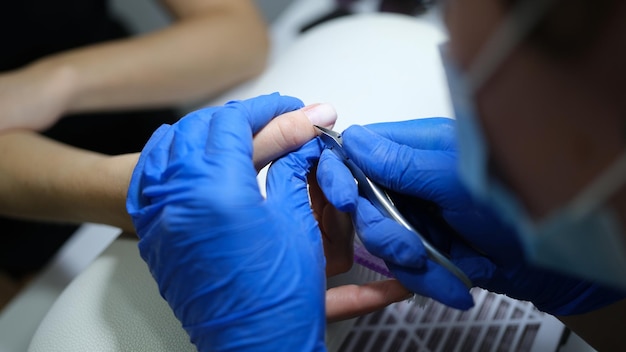 Manicurista en guantes de látex corta la cutícula del primer plano del dedo de los clientes de la esteticista que trabaja en el spa