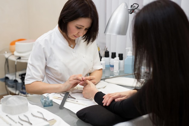 Manicurista haciendo manicura de hardware a una hermosa joven en el salón de spa Manicura de hardware