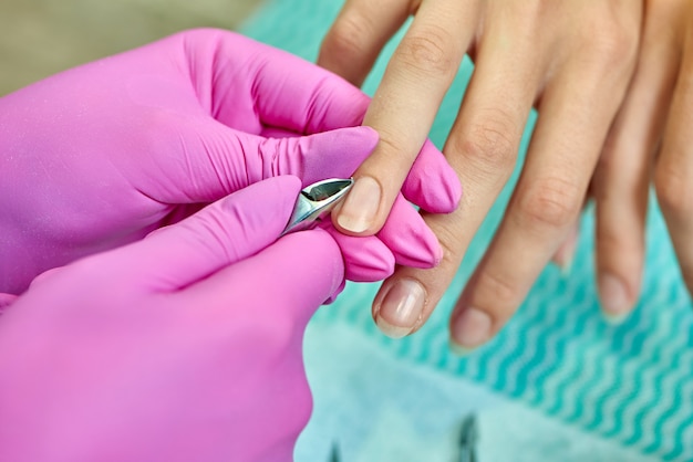 Manicurista profesional en guantes protectores con tijeras y corte de cutícula.