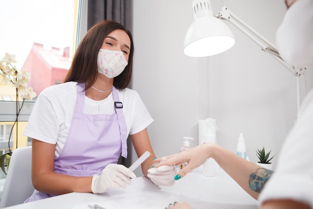 Manicurista profesional con mascarilla mientras trabaja durante la pandemia de coronavirus