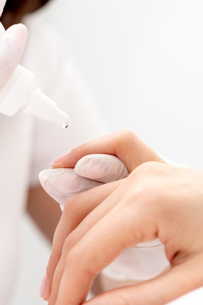 Manicurista profesional vertiendo aceite en las uñas manicura de mujer en salón de belleza.