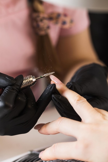 Una manicurista quita el esmalte en gel de las uñas usando un cortador de fresado hardware manicura primer recubrimiento ...