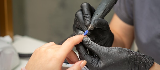 Manicurista quita el esmalte de uñas utiliza la máquina eléctrica de la lima de uñas durante la manicura en un salón de uñas.