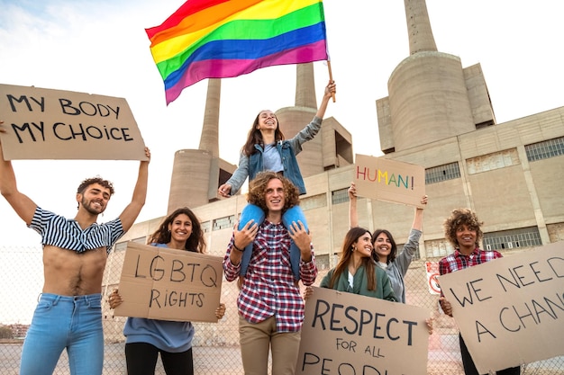 Manifestantes multirraciais manifestam-se por cartazes de posse de direitos LGTB e acenando a bandeira do arco-íris Conceito de diversidade e tolerância