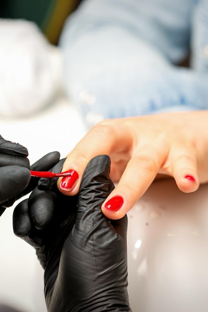 Maniküre-Lack-Malerei Nahaufnahme eines Maniküre-Meisters mit schwarzen Gummihandschuhen, der im Schönheitssalon roten Lack auf einen weiblichen Fingernagel aufträgt