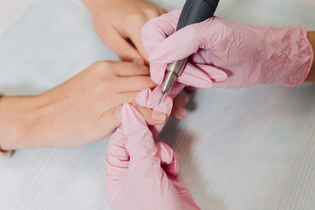 Maniküre-Prozess. Ein Meister in rosa Gummihandschuhen poliert Nägel mit einer elektrischen Nagelfeile. Weibliche Hände schließen.