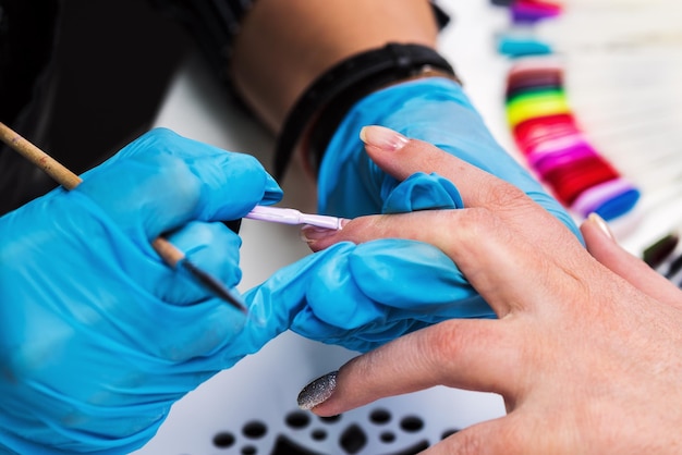 Maniküre trägt eine Schicht Gellack auf den Nagel des Kunden auf. Pinsel rosa Nagellack