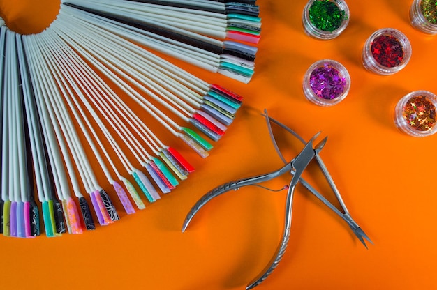 Maniküre- und Pediküre-Werkzeuge auf orangefarbenem Hintergrund Nagelfeile Schere Pinzette Drücker Zangen Quasten Medizinische Werkzeuge Draufsicht