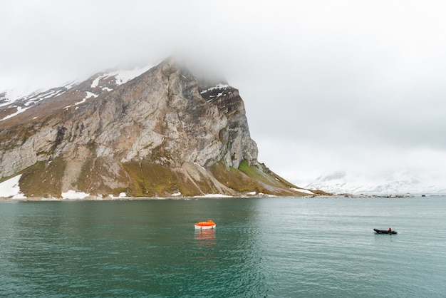Foto maniobra naranja bote salvavidas en el agua en las aguas del ártico, svalbard. abandonar el simulacro de barco. entrenamiento en bote salvavidas. hombre al agua taladro.