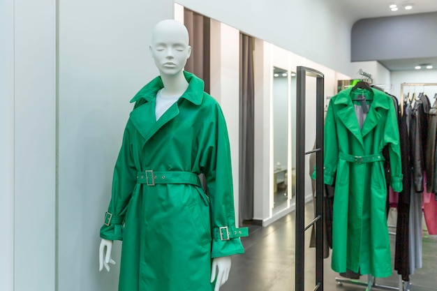 Maniquí femenino en una gabardina verde de moda en una ventana boutique Colección de ropa elegante y femenina Vista frontal