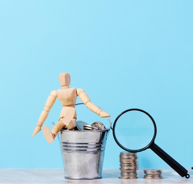 Un maniquí de madera y monedas en un balde en miniatura sobre un fondo azul un concepto de subsidio de altos ingresos