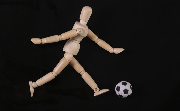Maniqui de marionetas de madera jugando con una pelota de fútbol aislado sobre fondo negro
