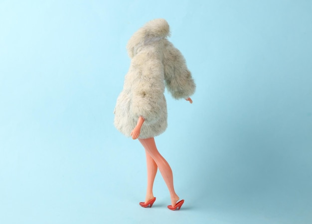 Maniquí de muñeca con abrigo de piel cálido sobre un fondo azul Disparo de moda minimalista Arte conceptual