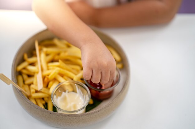 Manita sosteniendo papas fritas Dip en salsa de tomate en la mesa