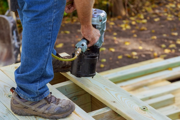 Manitas instalando pisos de madera en el patio, trabajando con una pistola de clavos para clavar