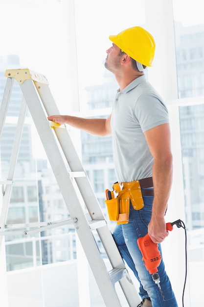 Manitas con máquina de taladro escalera de escalada en la construcción