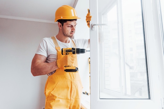 Manitas en uniforme amarillo instala una nueva ventana usando un destornillador automático Concepción de renovación de la casa