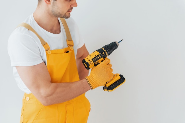 Manitas en uniforme amarillo de pie contra la pared blanca con destornillador automático Concepción de renovación de la casa