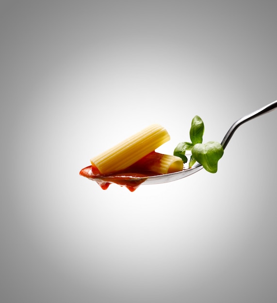 Foto manjericão perto de molho de macarrão e tomate em uma colher