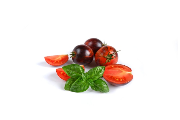 Manjericão verde italiano fresco e vermelho com tomates inteiros e cortados escuros em um fundo branco.