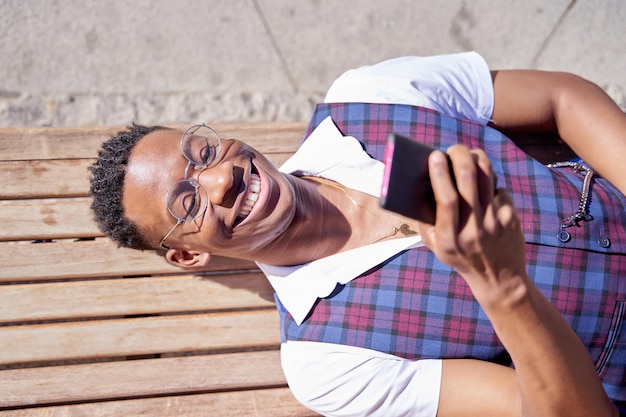 Mann afroamerikanischer Geschäftsmann, der auf einer Bank liegt und sich nach der Arbeit ausruht, benutzt ein Mobiltelefon