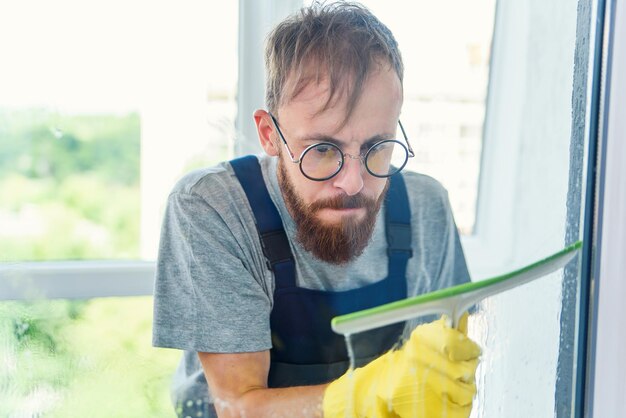 Foto mann als professioneller reiniger in blauer uniform wäscht fenster mit gummibürste drinnen