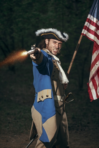 Mann als Soldat des Unabhängigkeitskrieges verkleidet USA zielt von Pistole mit Flagge