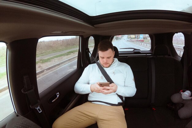 Mann am Auto hinten sitzt mit Telefon Taxi App Copy Space Road Trip mit Gürtel anschnallen