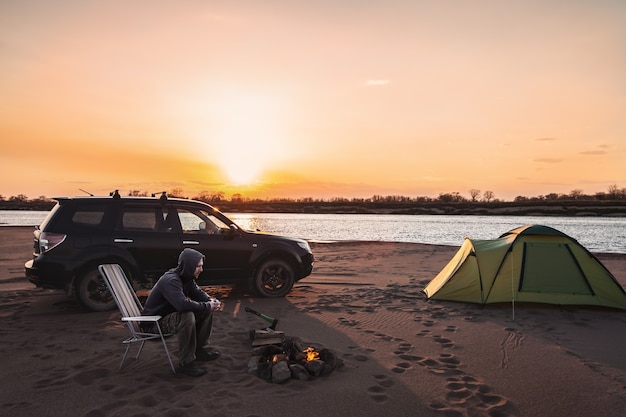 Mann am Lagerfeuer bei Sonnenuntergang auf einer Sandflussbank