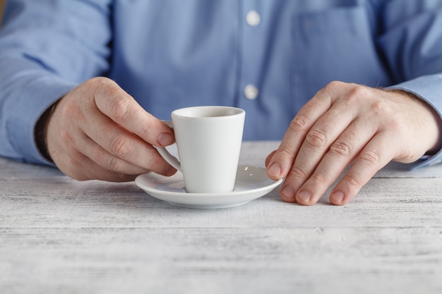 Mann am Tisch hält eine Tasse Espresso in der Hand