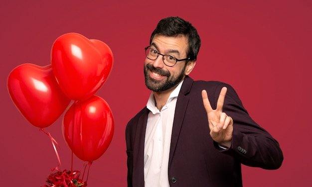 Mann am Valentinstag lächelnd und Siegeszeichen mit beiden überreicht roten Hintergrund