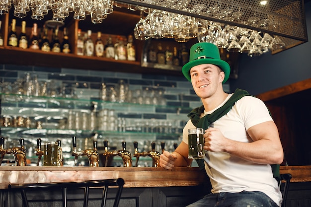 Mann an der Bar mit Bier. Guy feiert den St. Patrick's Day. Mann in einem grünen Hut.