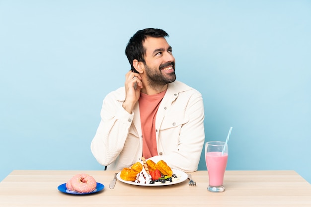 Mann an einem Tisch, der Frühstückswaffeln und einen Milchshake denkt eine Idee hat