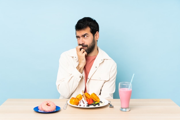 Mann an einem Tisch, der Frühstückswaffeln und einen Milchshake hat, der Zweifel hat