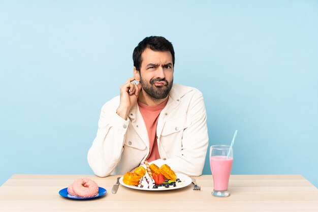 Mann an einem Tisch, der Frühstückswaffeln und einen Milchshake hat, der Zweifel hat