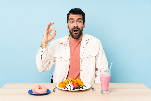 Mann an einem Tisch mit Frühstückswaffeln und einem Milchshake überrascht und zeigt ok Zeichen