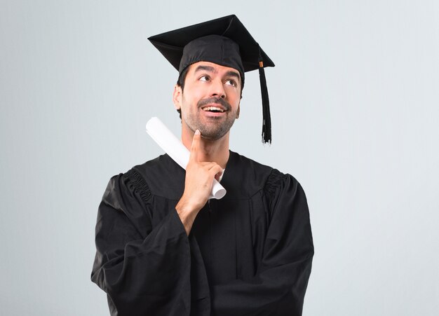 Mann an seinem Abschlusstag Universität, die eine Idee auf grauem Hintergrund steht und denkt