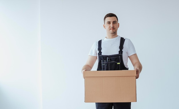 Mann Arbeiter in schwarzer Uniform halten große Kiste beim Blick auf die Kamera Umzug in eine neue Wohnung