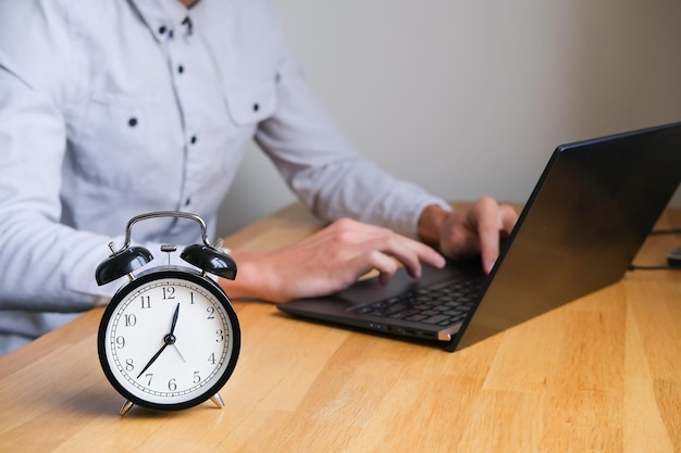 Mann arbeitet am Laptop mit Wecker auf dem Tisch