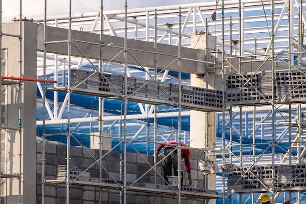 Mann arbeitet auf der Baustelle mit Gerüst und Gebäude mit Himmelshintergrund, Gerüst für Baufabrik