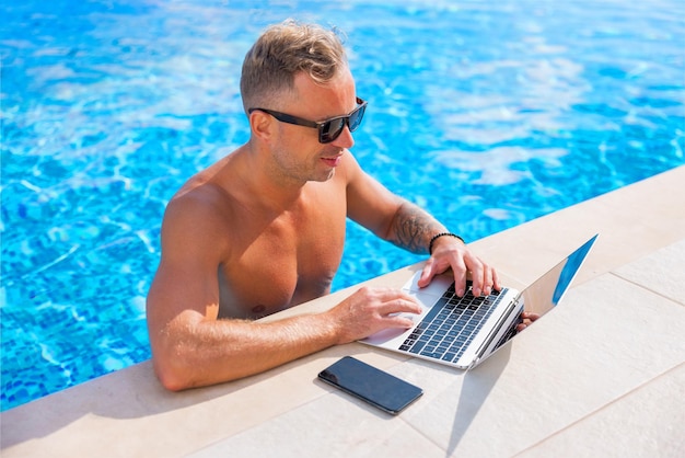 Mann arbeitet im Urlaub mit Laptop am Pool