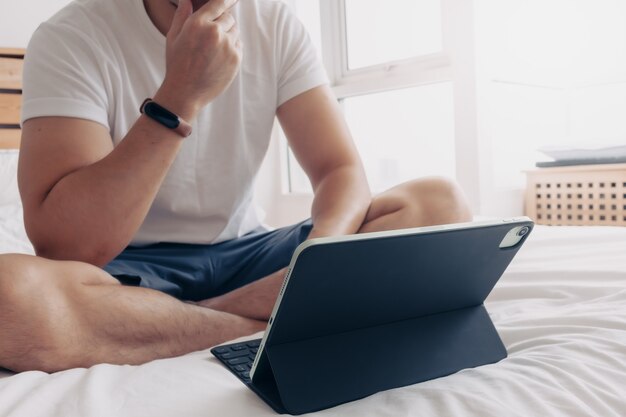 Mann arbeitet mit Tablet und Kaffee im Schlafzimmerkonzept der Arbeit von zu Hause aus