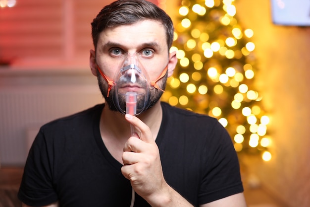 Mann atmet mit einem Lungeninhalationsgerät vor dem Hintergrund der Weihnachtsbeleuchtung ein
