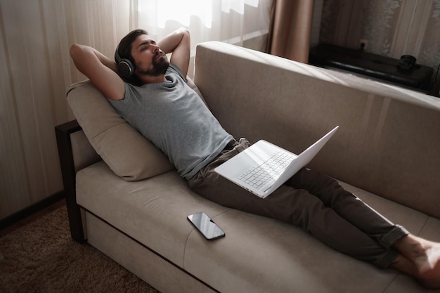 Mann auf dem Sofa mit Kopfhörern und Notebook zu Hause